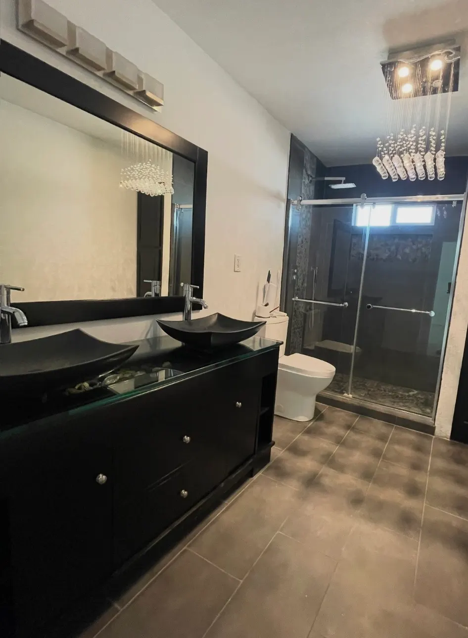 Modern bathroom with black double vanity, vessel sinks, large mirror, glass shower, and crystal light fixtures.