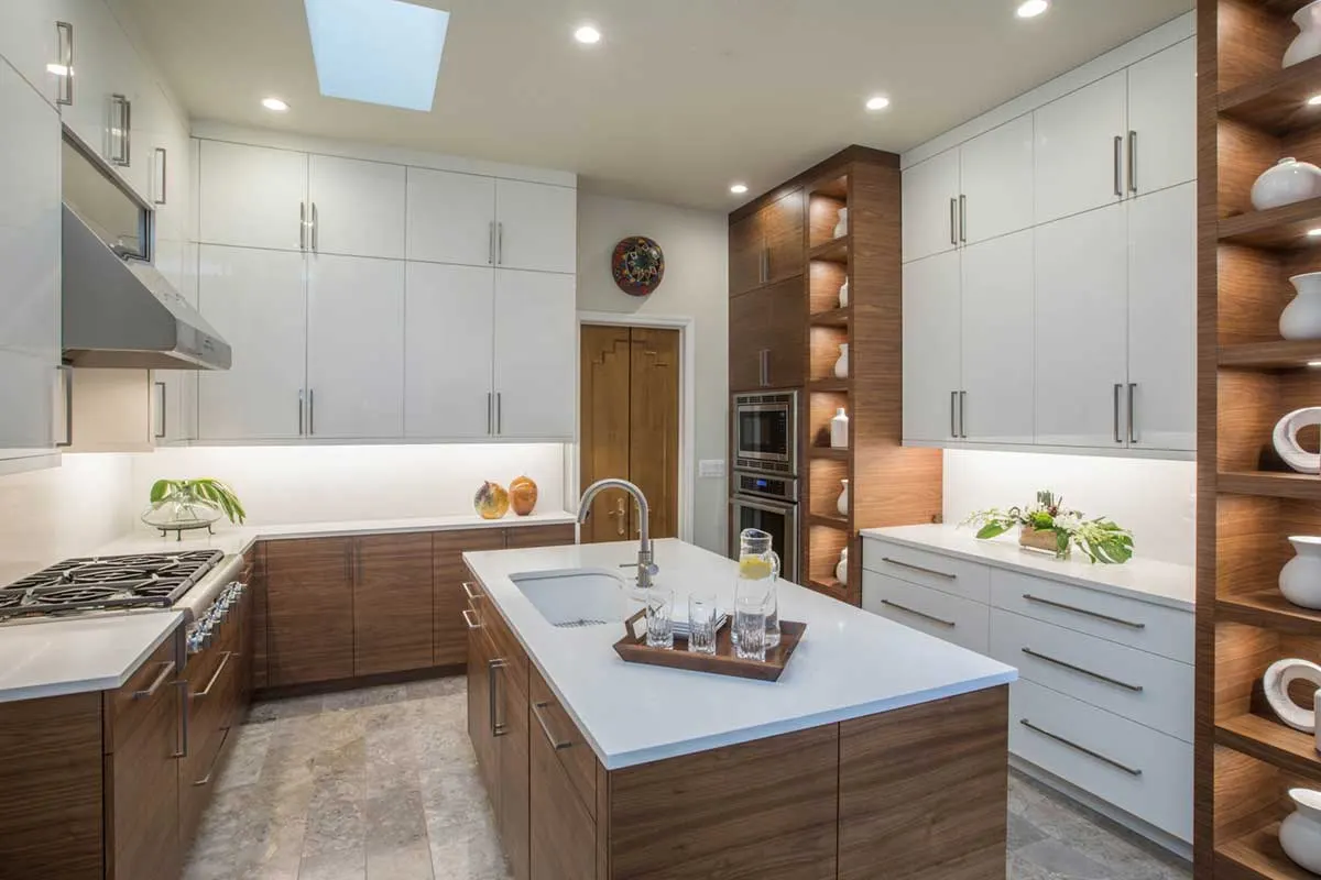 Modern kitchen with white upper cabinets, wood grain lower cabinets and island, quartz countertops, and stone tile floor.