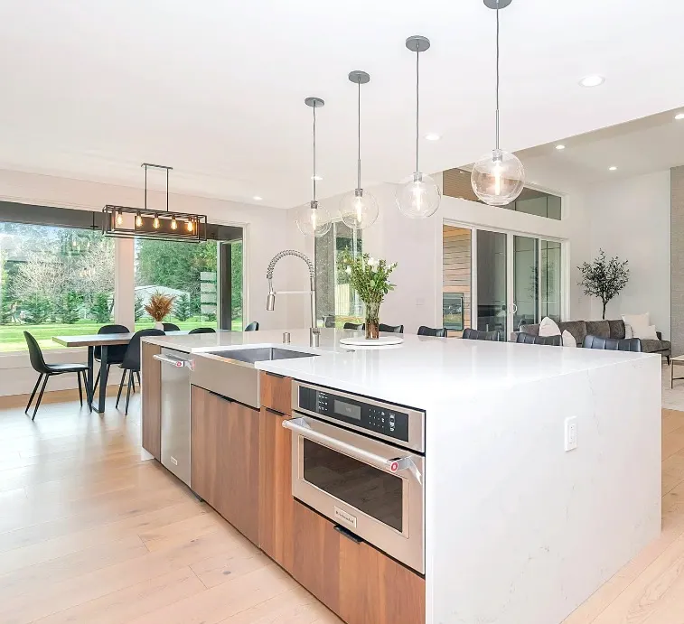 Modern open-concept kitchen with large white quartz island, wood cabinetry, stainless appliances, and pendant lights.