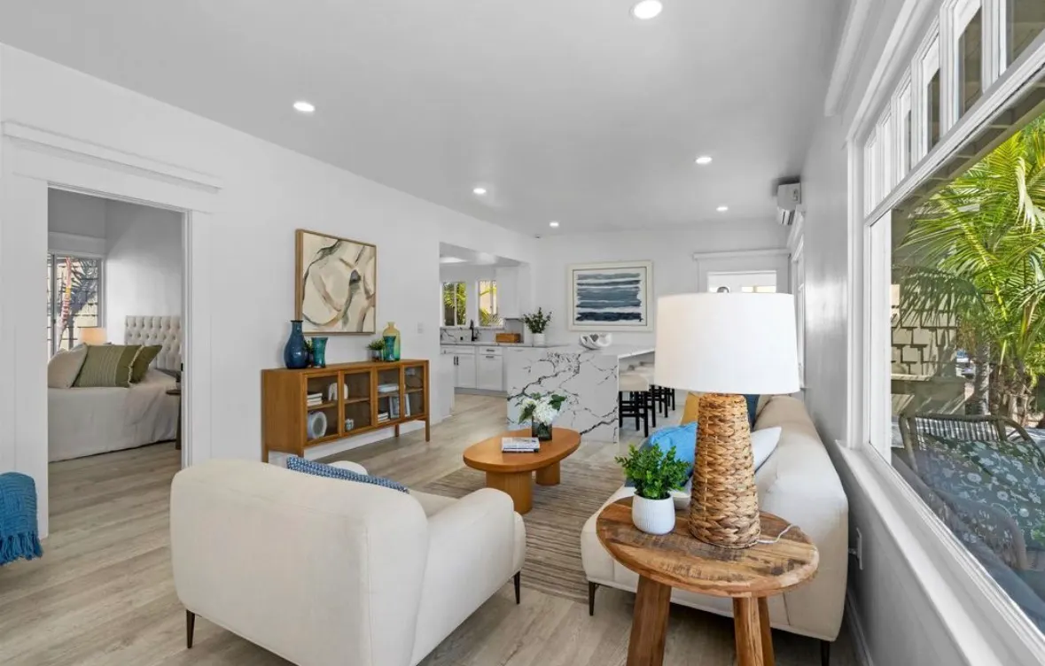 Bright open-concept living room and kitchen remodel featuring light wood floors, white walls, and modern furniture.