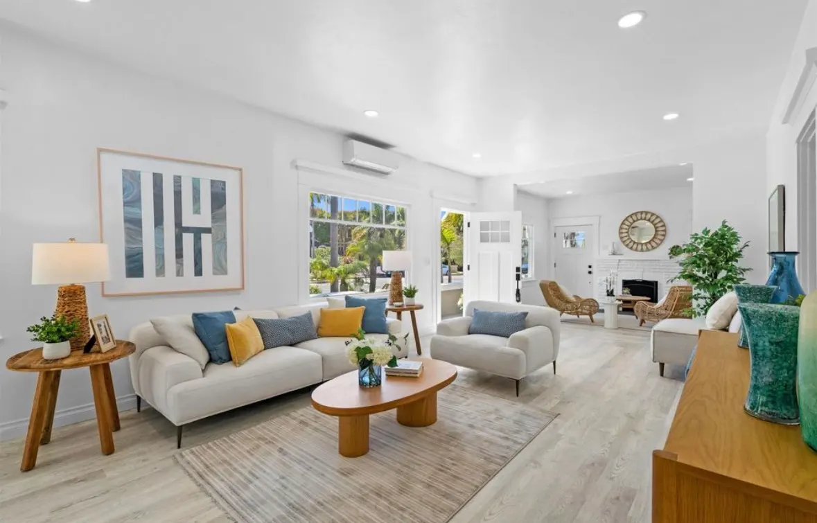 Bright living room remodel with white walls, light wood flooring, modern sofa, colorful pillows, and large windows.