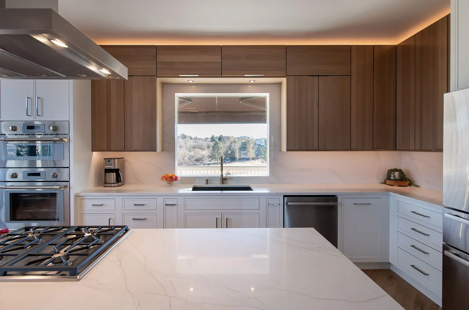 Modern kitchen with white island, dark wood and white cabinetry, marble countertops, stainless steel appliances, and large window.