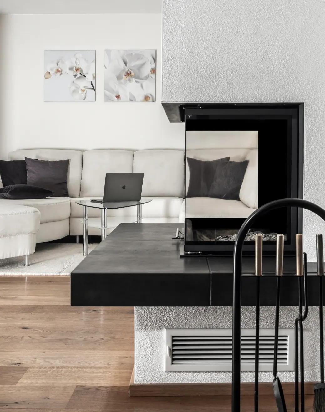 Modern living room with a sleek black fireplace, light wood flooring, a white sectional sofa, and minimalist decor.