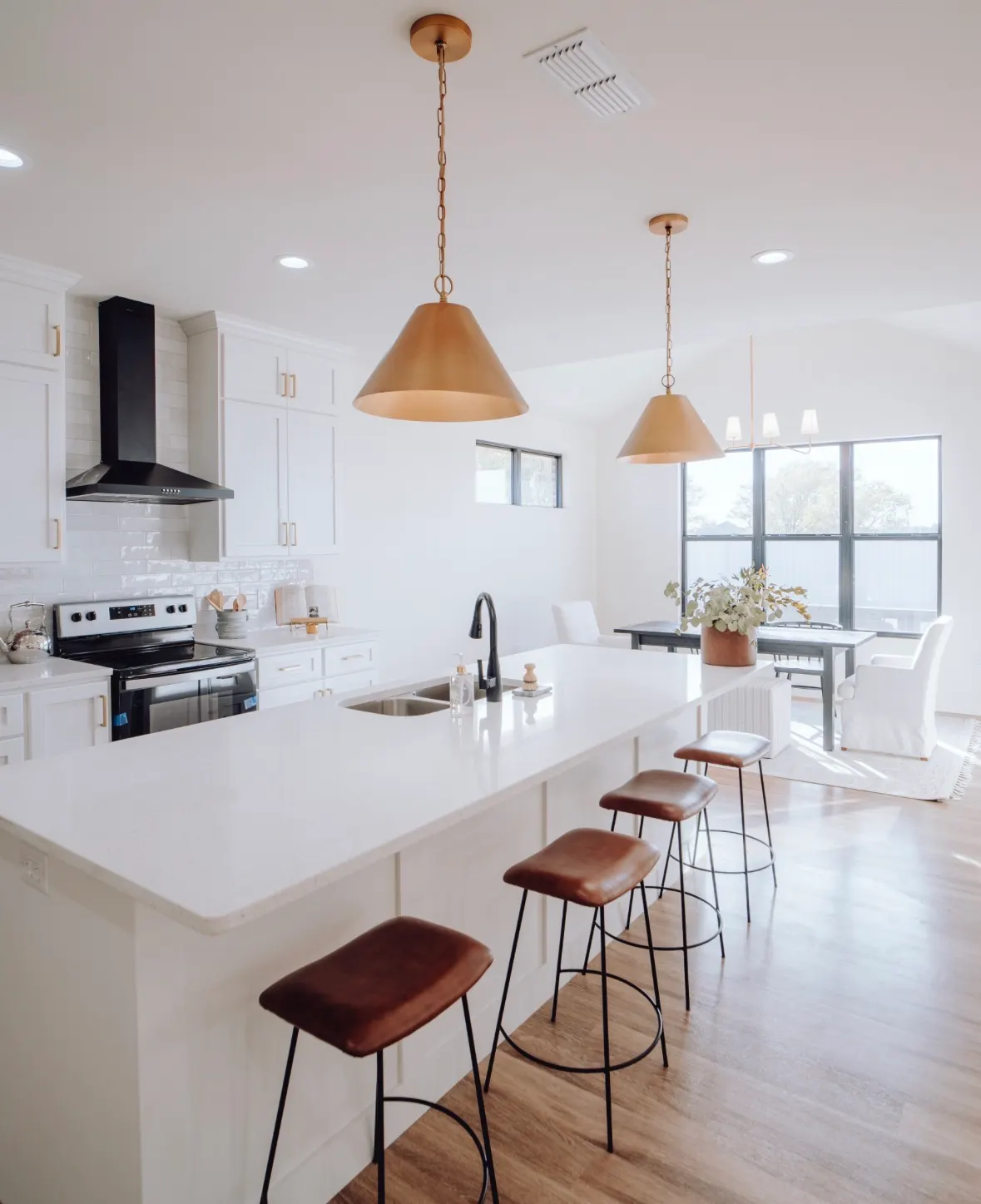 Modern kitchen with white shaker cabinets, quartz countertops, brass pendants, and wood-look flooring.