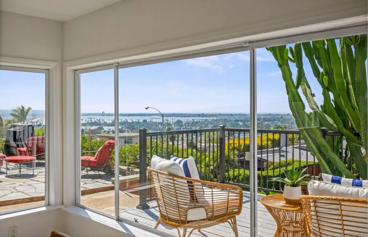 Patio with comfortable wicker chairs, striped pillows, and sweeping ocean views under blue sky.