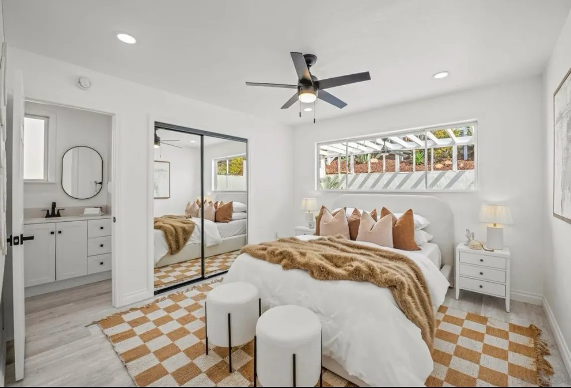 Modern bedroom with white walls, a bed featuring a brown throw blanket, and a checkered rug.