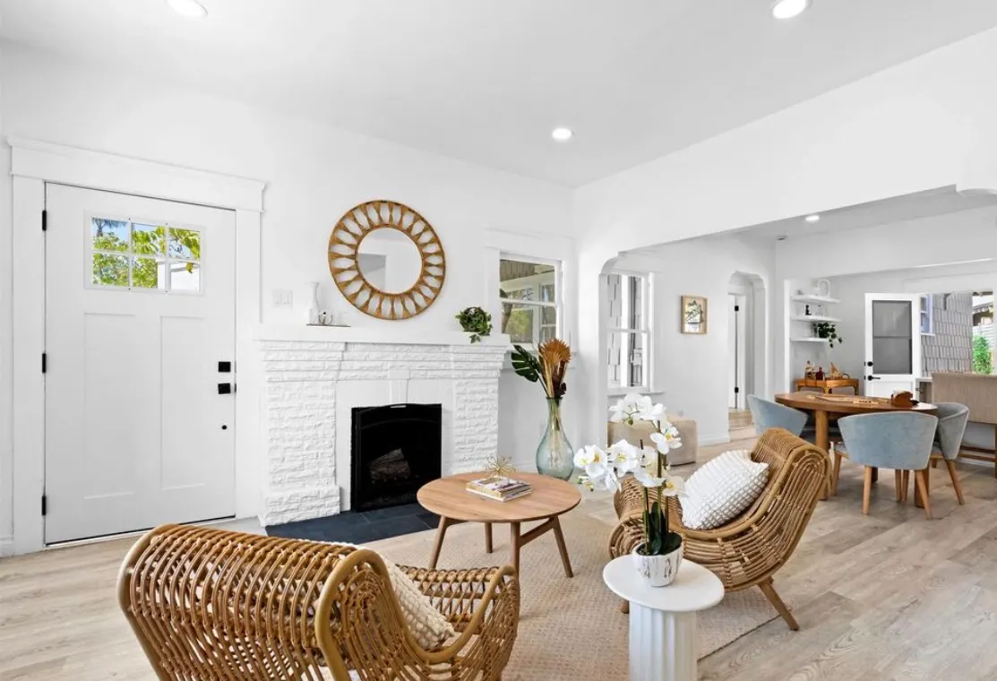 Bright living room remodel with white brick fireplace, rustic wood mirror, wicker chairs, and light flooring.
