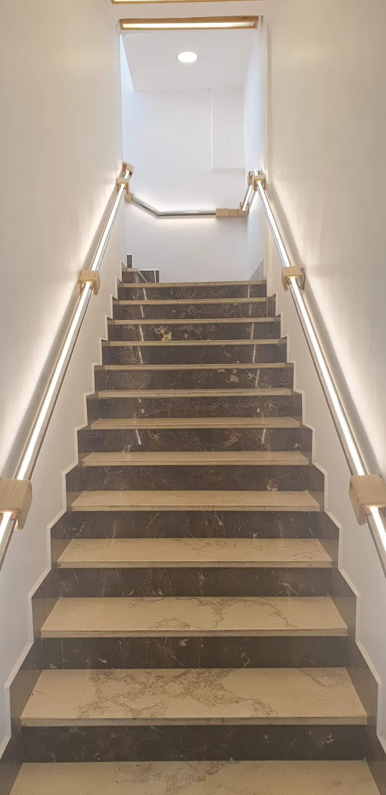 Modern staircase with two-tone marble treads and risers, illuminated by linear LED handrails.