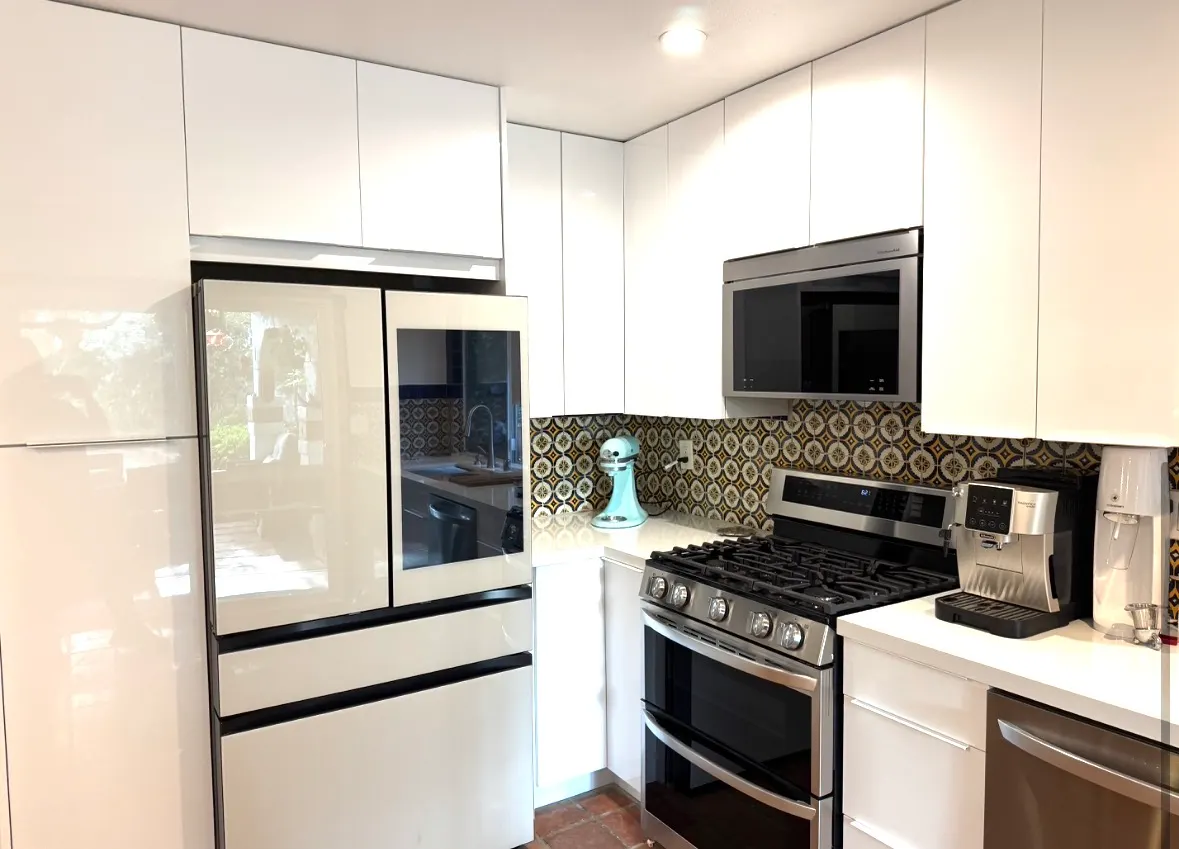 Modern kitchen with white glossy cabinets, unique patterned tile backsplash, stainless steel appliances, and white countertops.