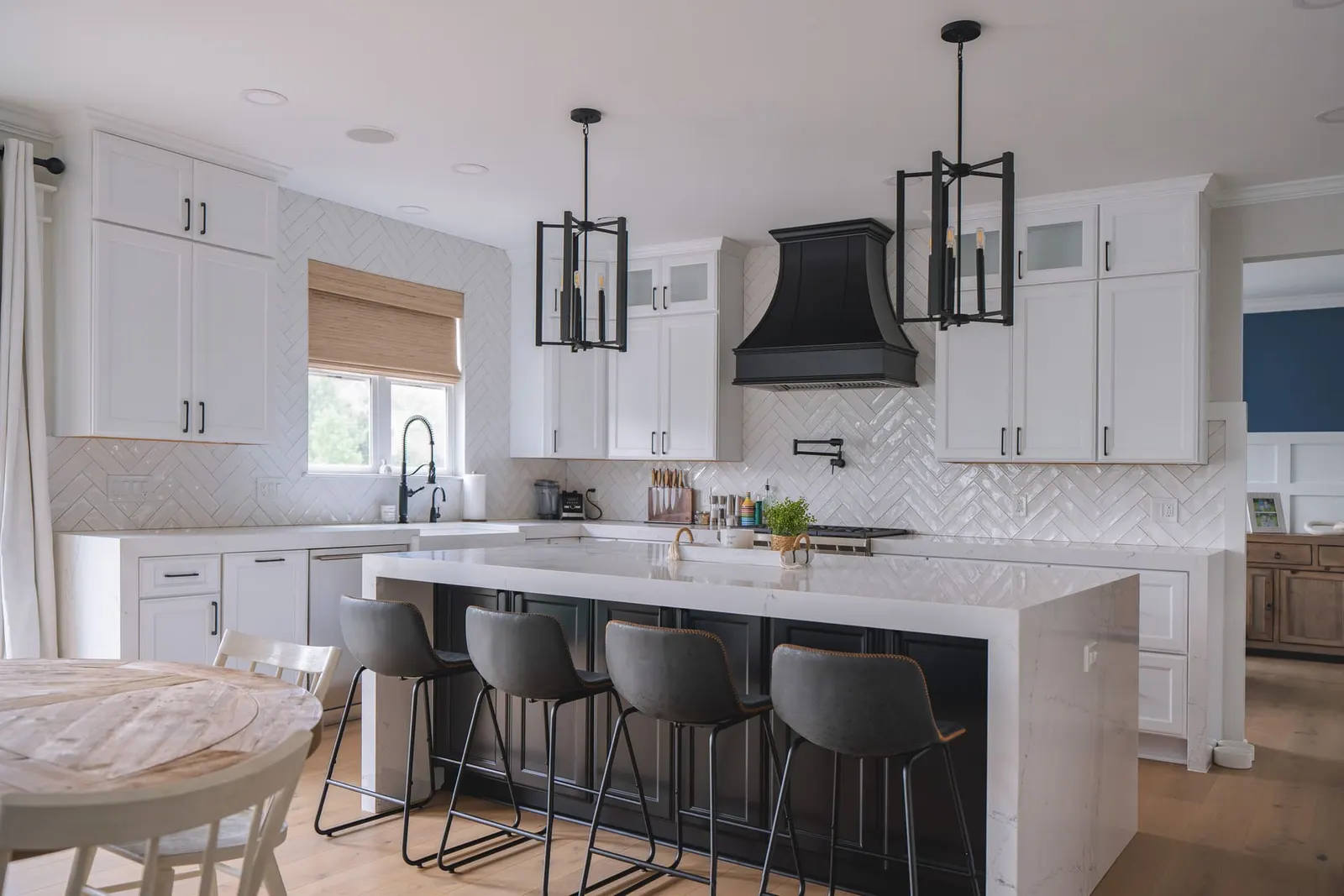 Modern kitchen with white shaker cabinets, herringbone subway tile, dark island, gold accents, and black light fixtures.