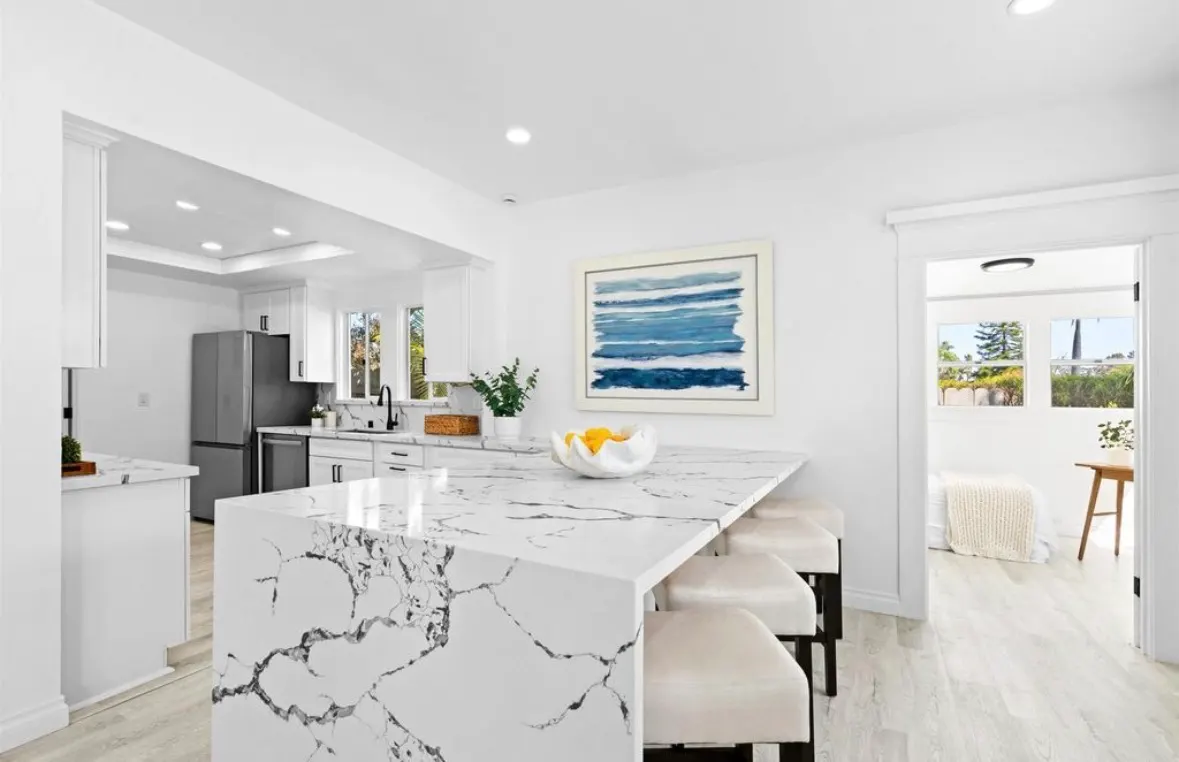 Modern kitchen remodel featuring a large white marble island with seating and new stainless steel appliances.