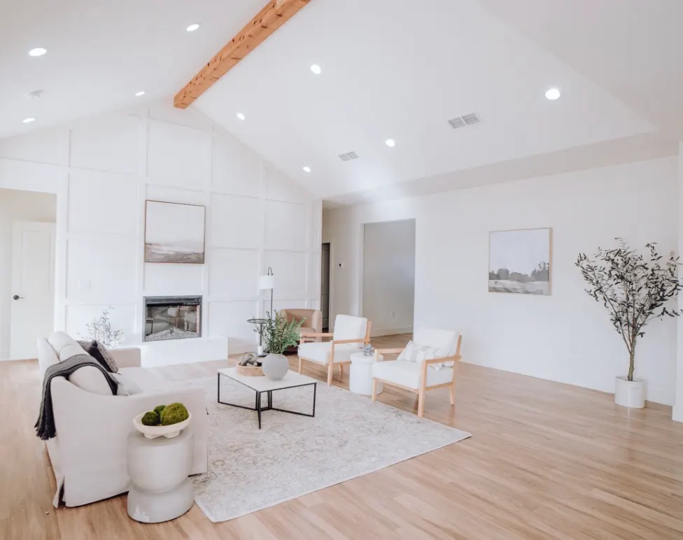 Bright living room with vaulted ceiling, exposed beam, modern fireplace, white board and batten walls, and light hardwood floors.