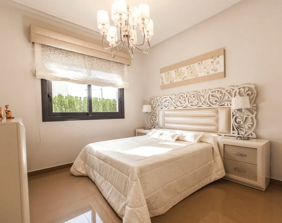 Elegant white bedroom with carved headboard, shiny tile floor, brown window frame, and stylish chandelier.
