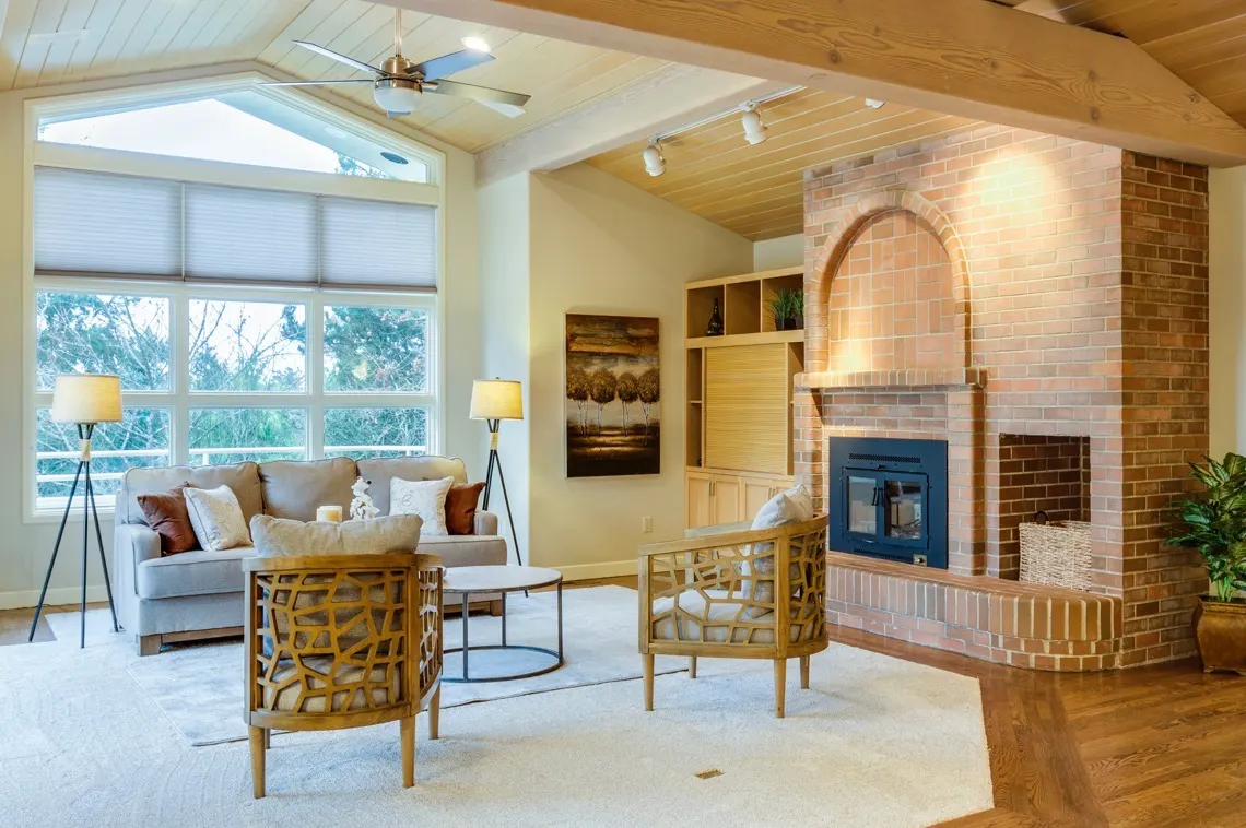Warm and inviting living room with large windows, brick fireplace, wood ceilings, and contemporary furniture.