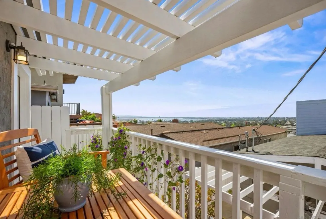 White pergola and railing on a wooden balcony with a scenic ocean view.