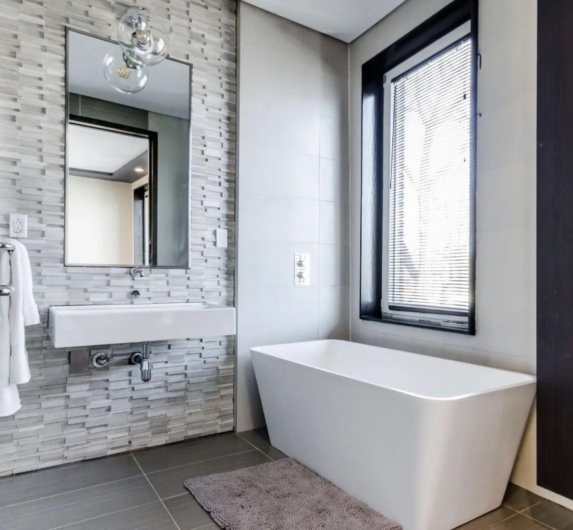 Modern bathroom remodel featuring a freestanding bathtub, vessel sink, geometric subway tile backsplash, and large window.