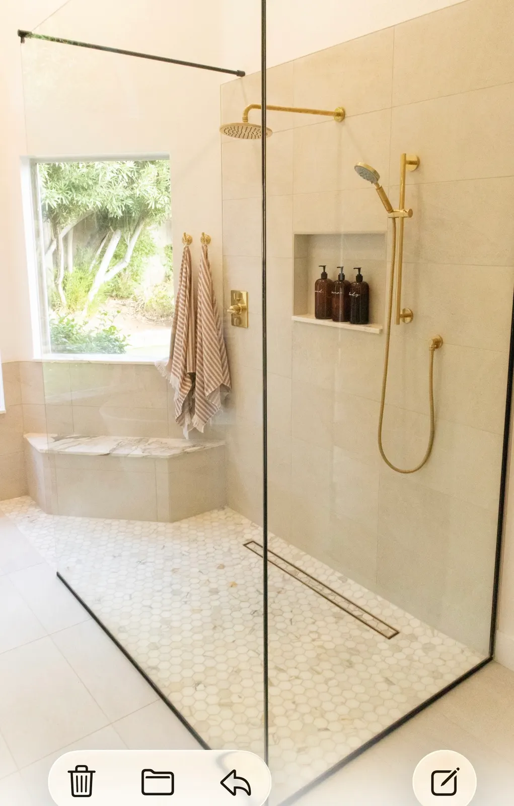 Modern shower with white hexagon tile floor, light beige wall tile, brass fixtures, and built-in bench.