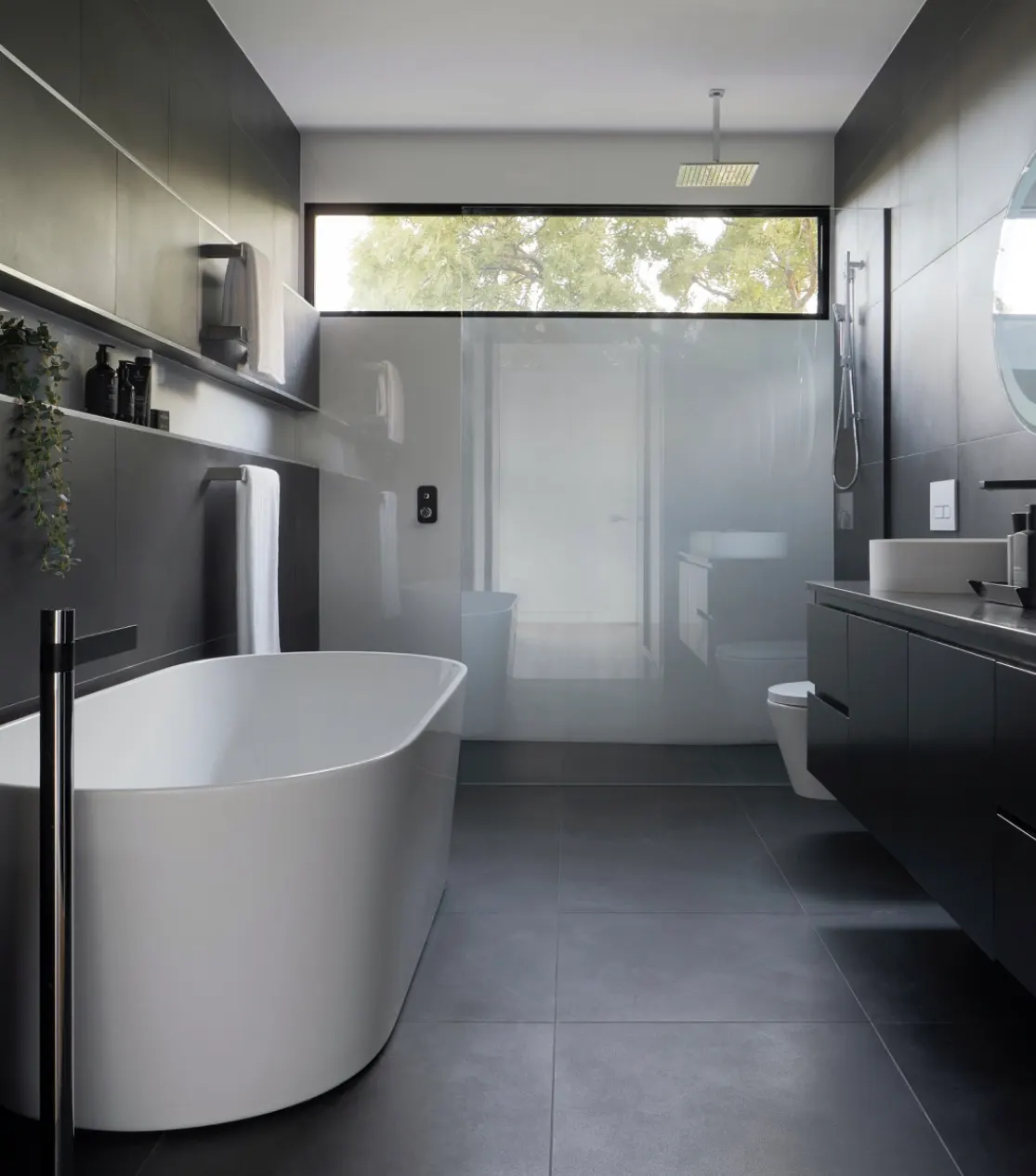 Modern bathroom remodel with freestanding tub, dark finishes, and a spacious glass shower in a gray interior.