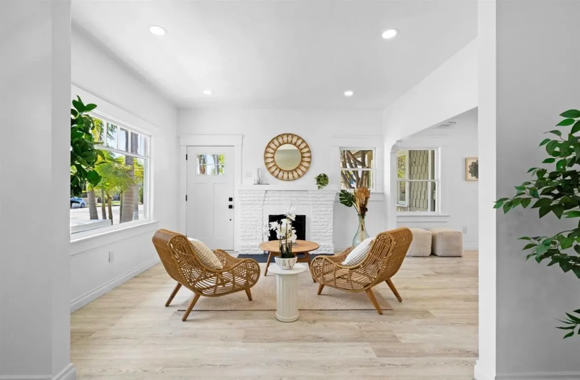 Brightly lit living room with white walls, light wood flooring, and a white brick fireplace.