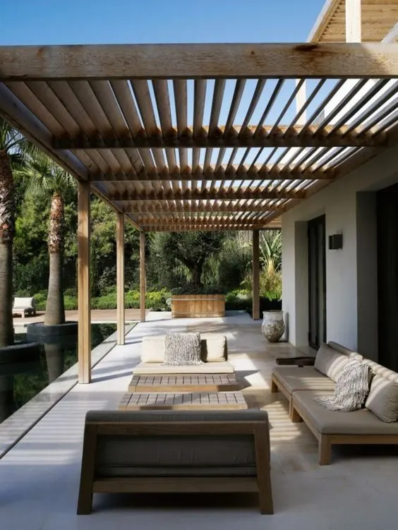 Luxurious outdoor patio design featuring a wooden slatted pergola, modern outdoor seating, and lush landscaping.