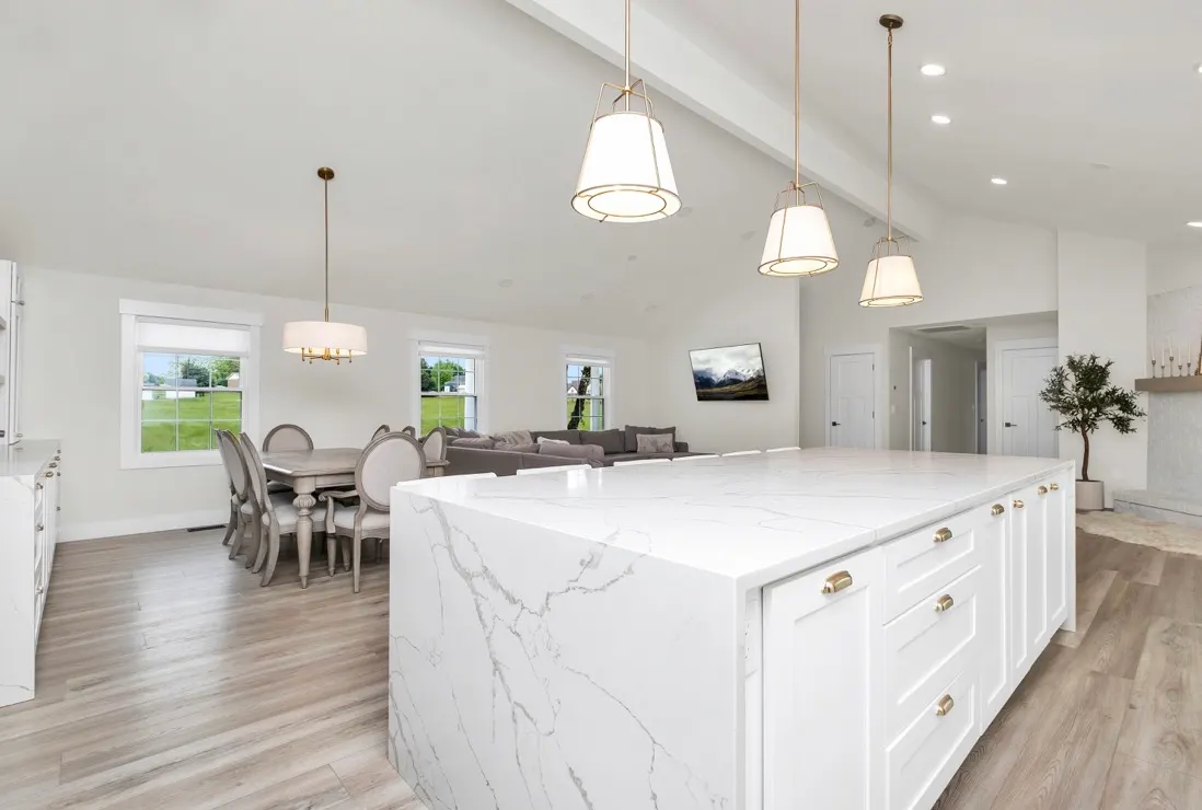 Bright open-concept kitchen and living area featuring a large white quartz island and light wood flooring.