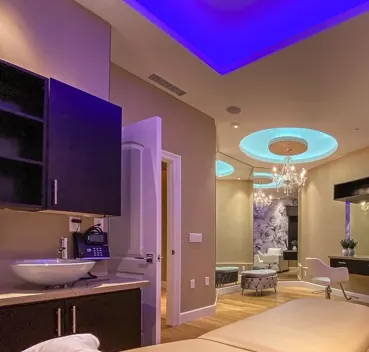 Luxury spa interior with purple and blue LED lighting, vanity, treatment bed, and modern fixtures.