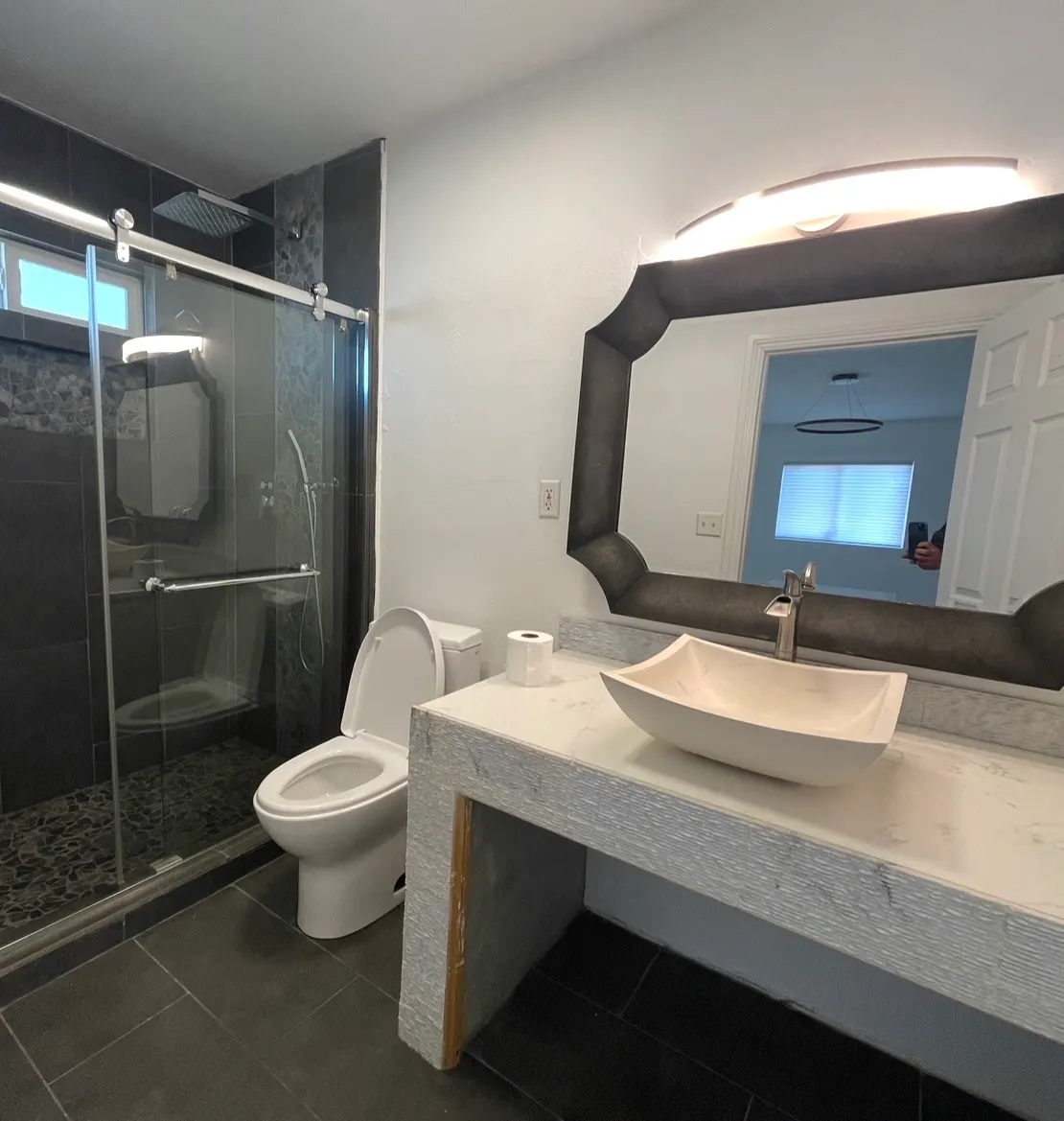 Modern bathroom remodel featuring a dark tile shower, white vessel sink, and textured vanity.