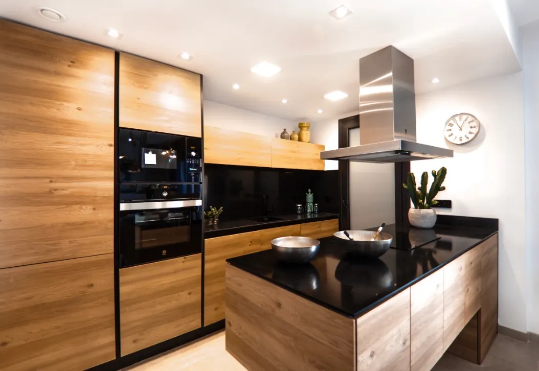 Modern kitchen with wood cabinets, black countertops, integrated appliances, and a stainless steel range hood.