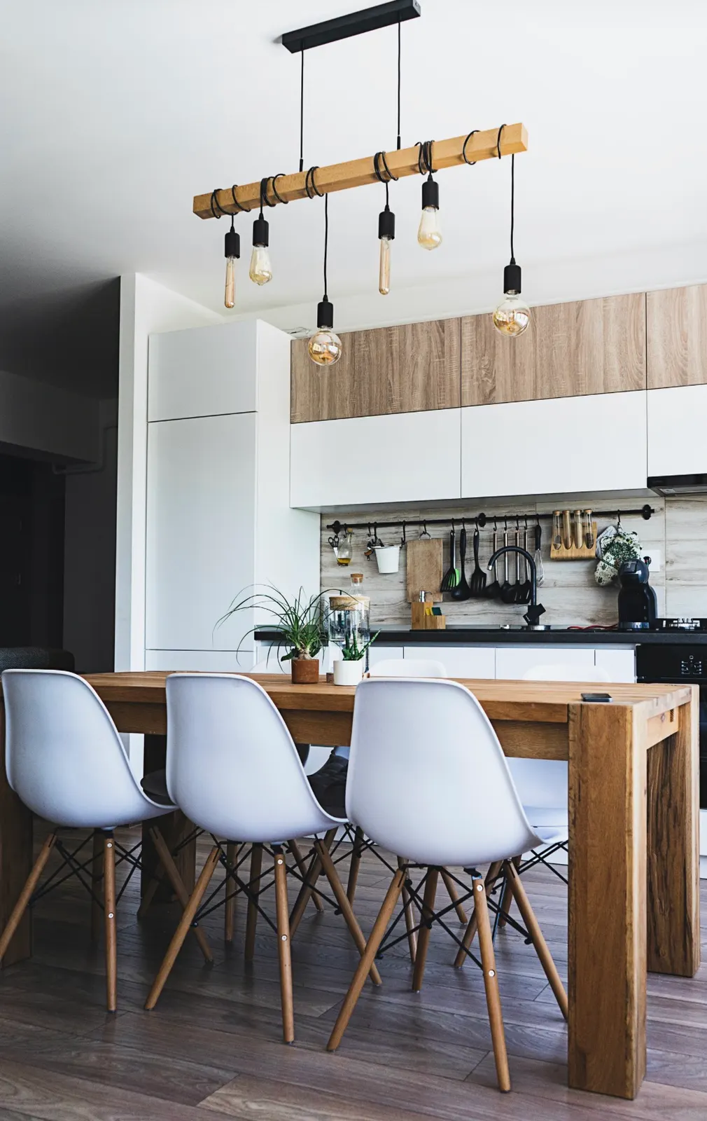 Modern open-concept kitchen dining area with white cabinets, wood accents, and a custom wooden chandelier.