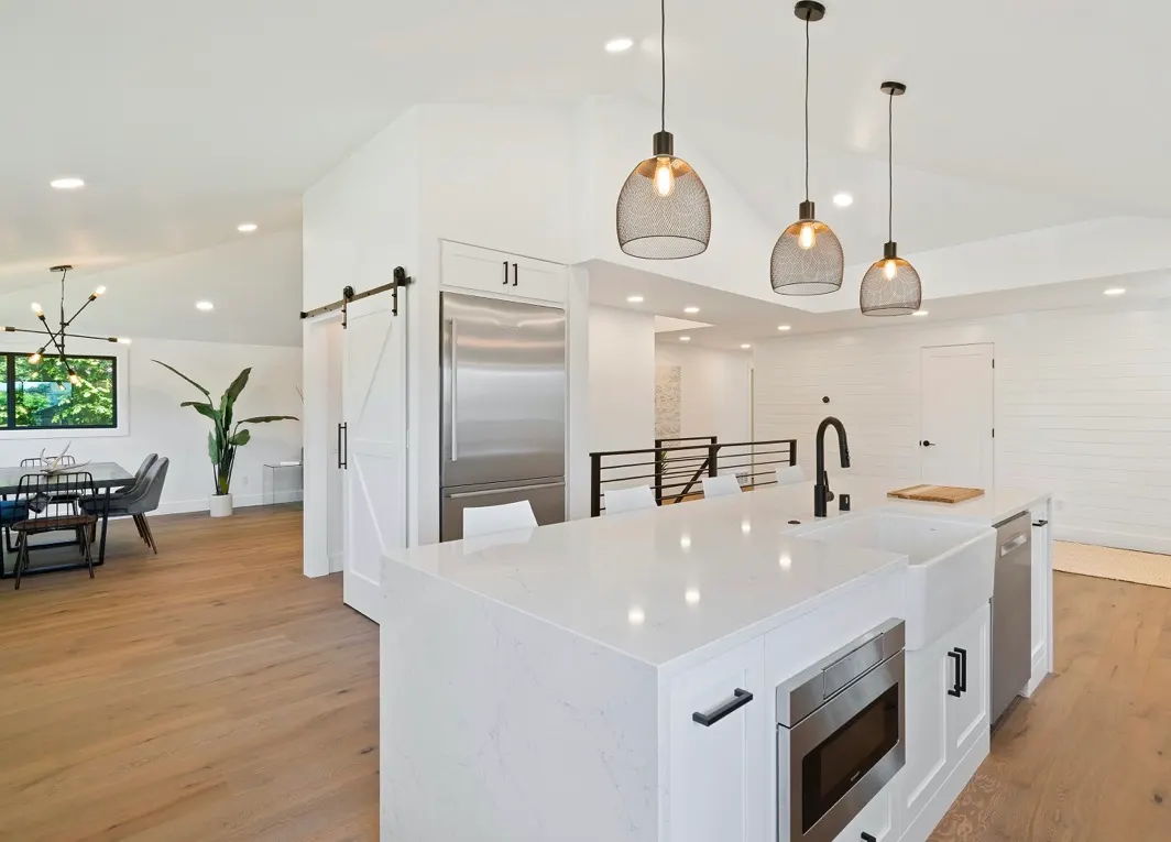 Modern open-concept kitchen with white cabinets, large island, stainless steel appliances, and wood flooring.
