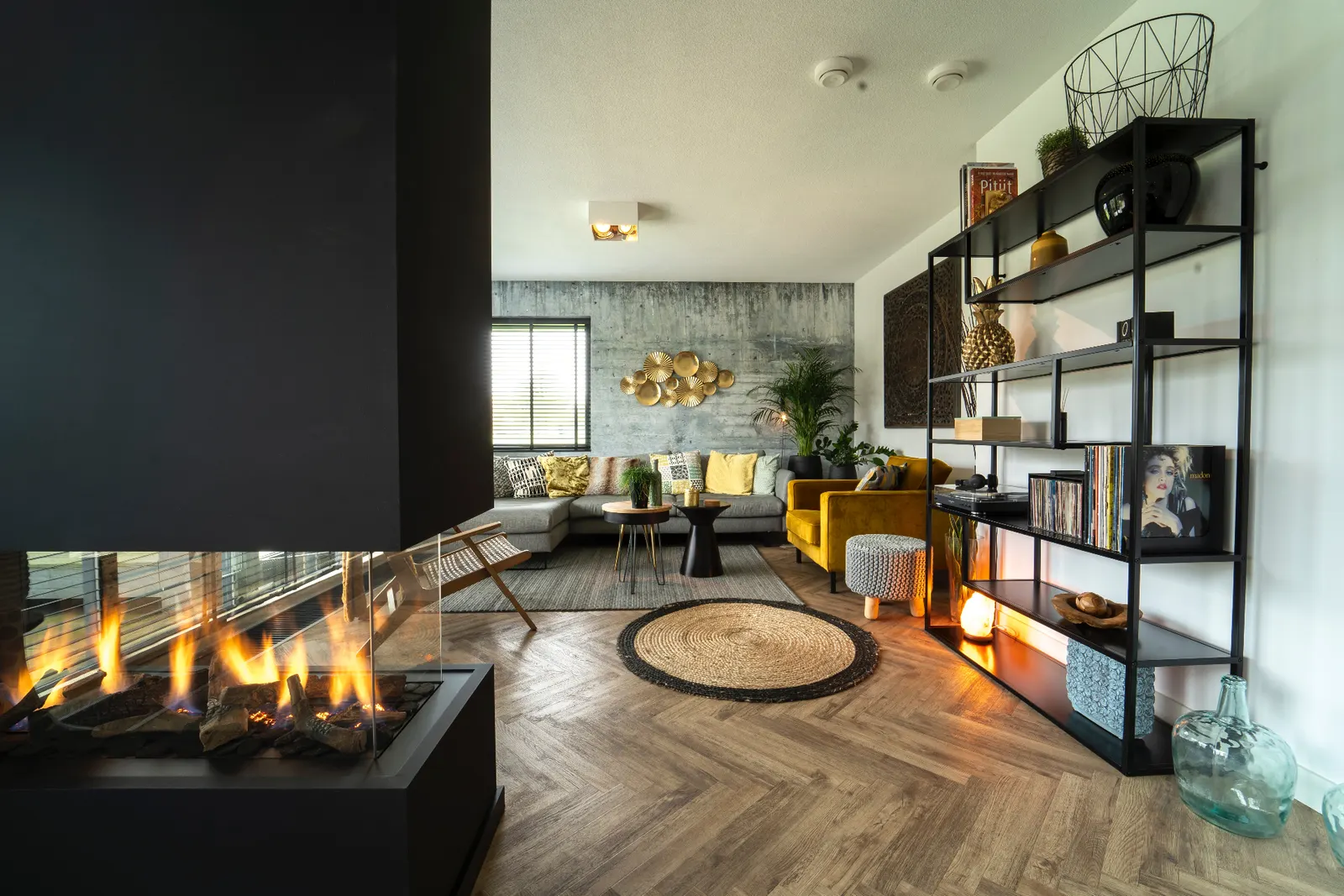 Modern living room remodel with a sleek black fireplace, concrete accent wall, and herringbone wood floor.