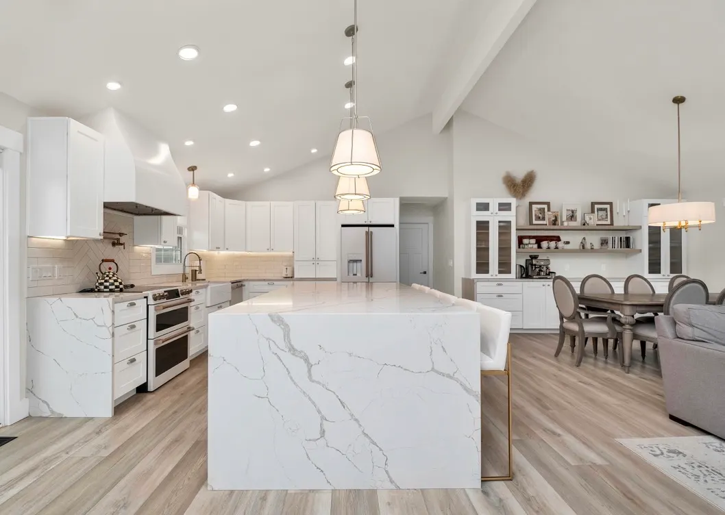 Modern kitchen with white shaker cabinets, white waterfall island, waterfall countertops, and wood flooring.