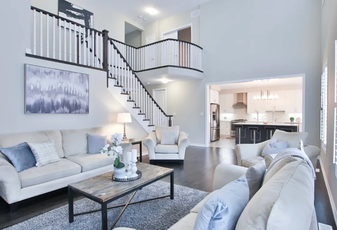 Spacious living room with light walls, dark wood flooring, white sofas, rustic coffee table, and a grand staircase.