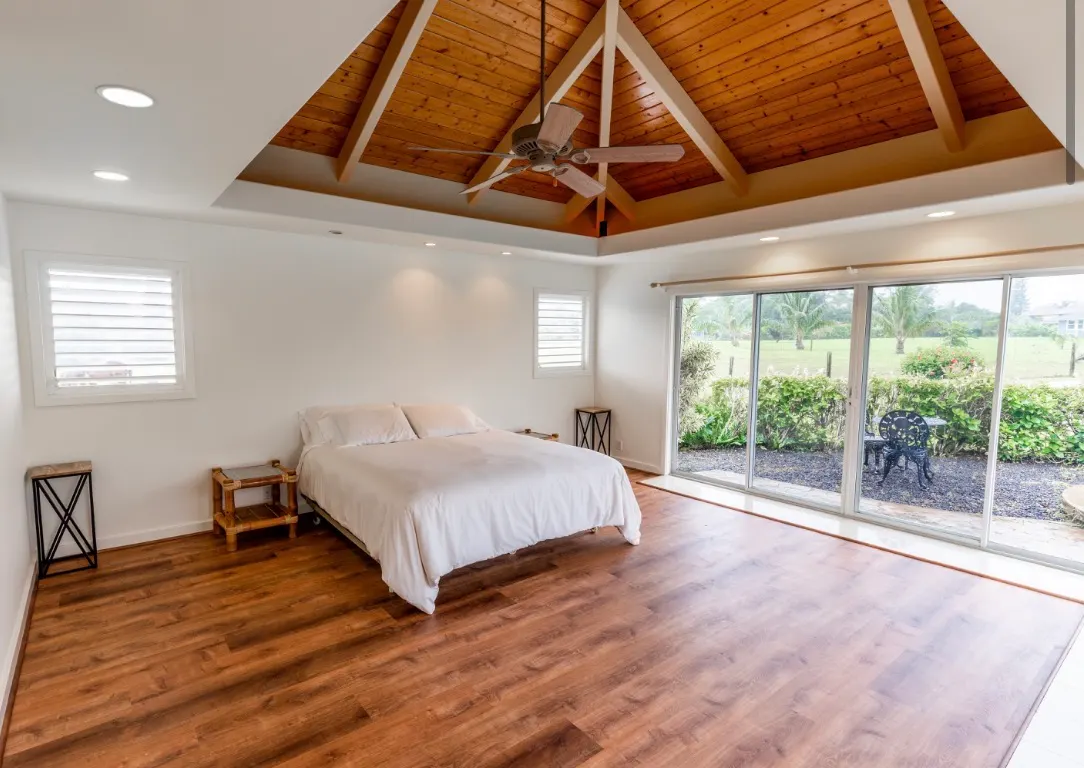 Modern bedroom with vaulted wooden ceiling, white walls, and large sliding glass doors opening to a patio.