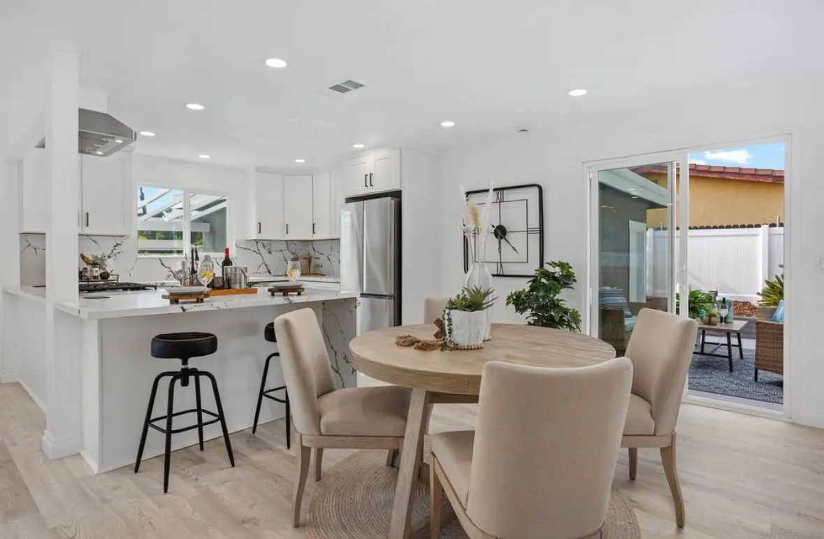 Modern open-concept kitchen with white cabinets, quartz countertops, stainless steel appliances, and adjacent dining area.