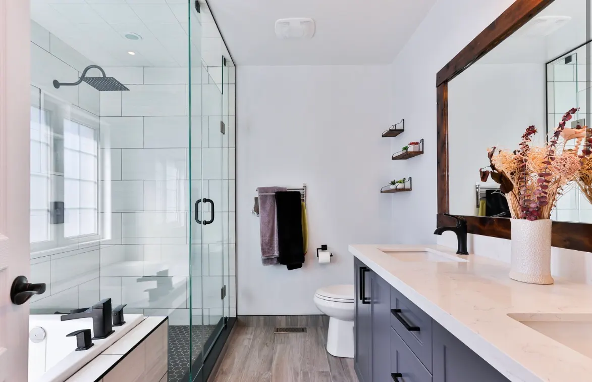 Modern bathroom with glass shower, white subway tile, double vanity, wood mirror, and dark fixtures.
