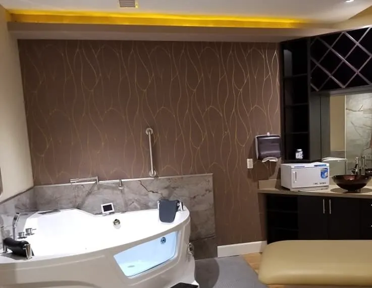 Luxurious bathroom featuring a large white corner jetted tub, elegant brown patterned wallpaper, and a dark wood vanity with vessel sink.