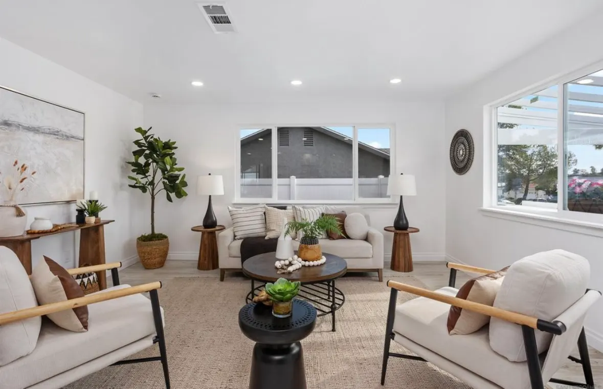 Bright living room with white walls, light sofa, modern armchairs, wood tables, and a large window.