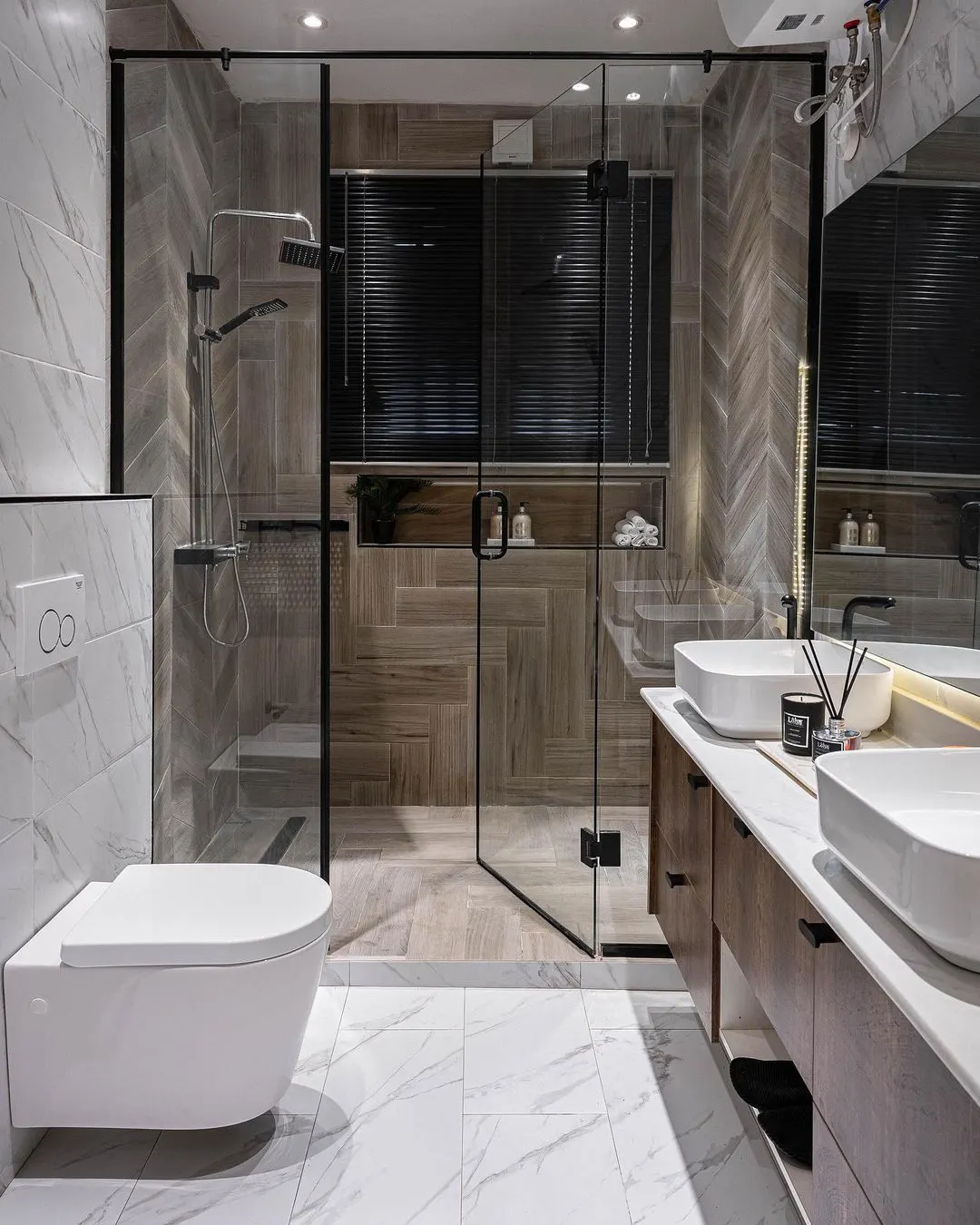 Modern bathroom remodel featuring a glass shower, floating toilet, dual vanity, and elegant wood-effect chevron tiles.