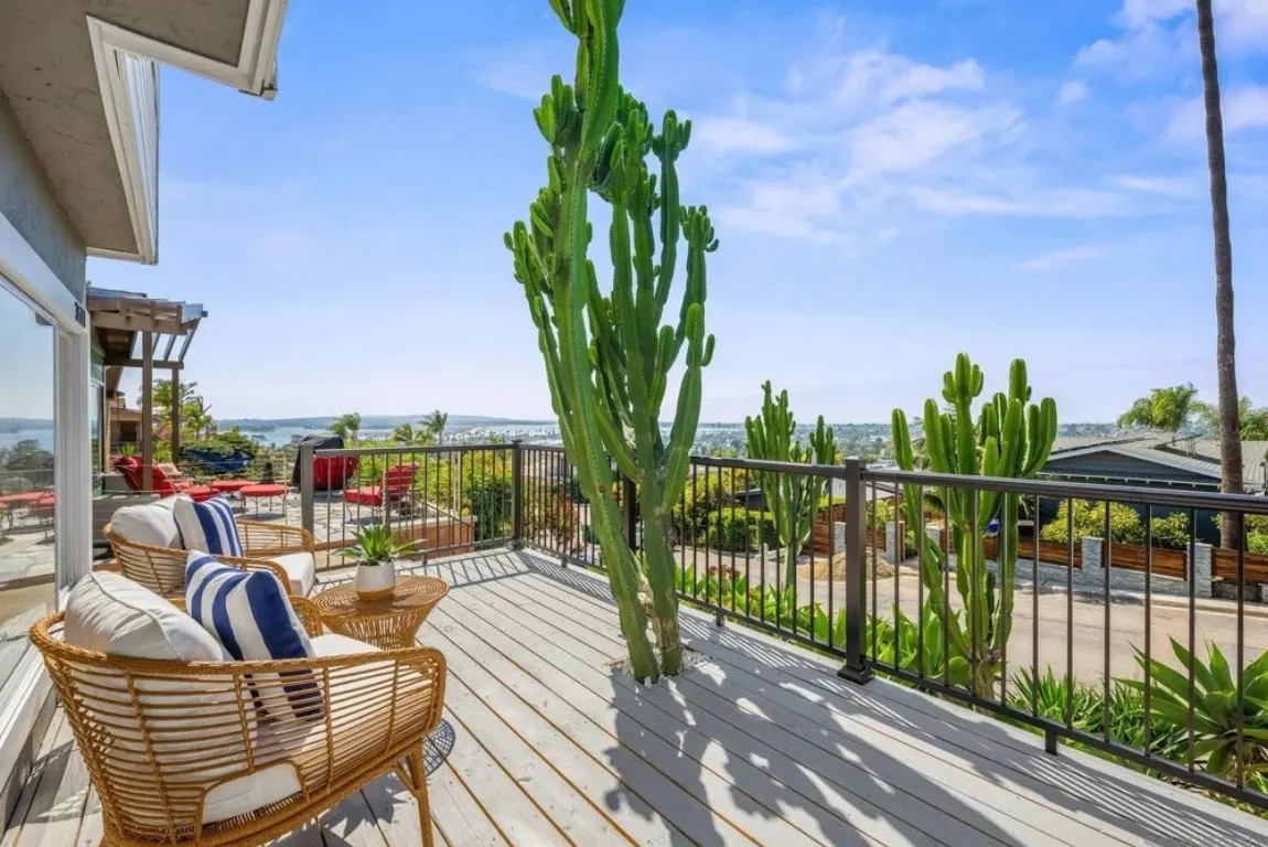 Spacious elevated outdoor deck with wicker chairs, a tall cactus, and views of the ocean.