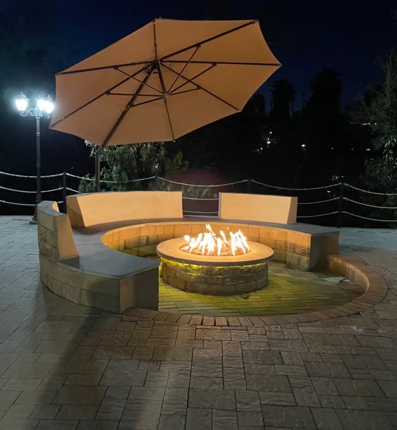 Stunning outdoor patio with a circular gas fire pit, built-in curved seating, and a large umbrella.
