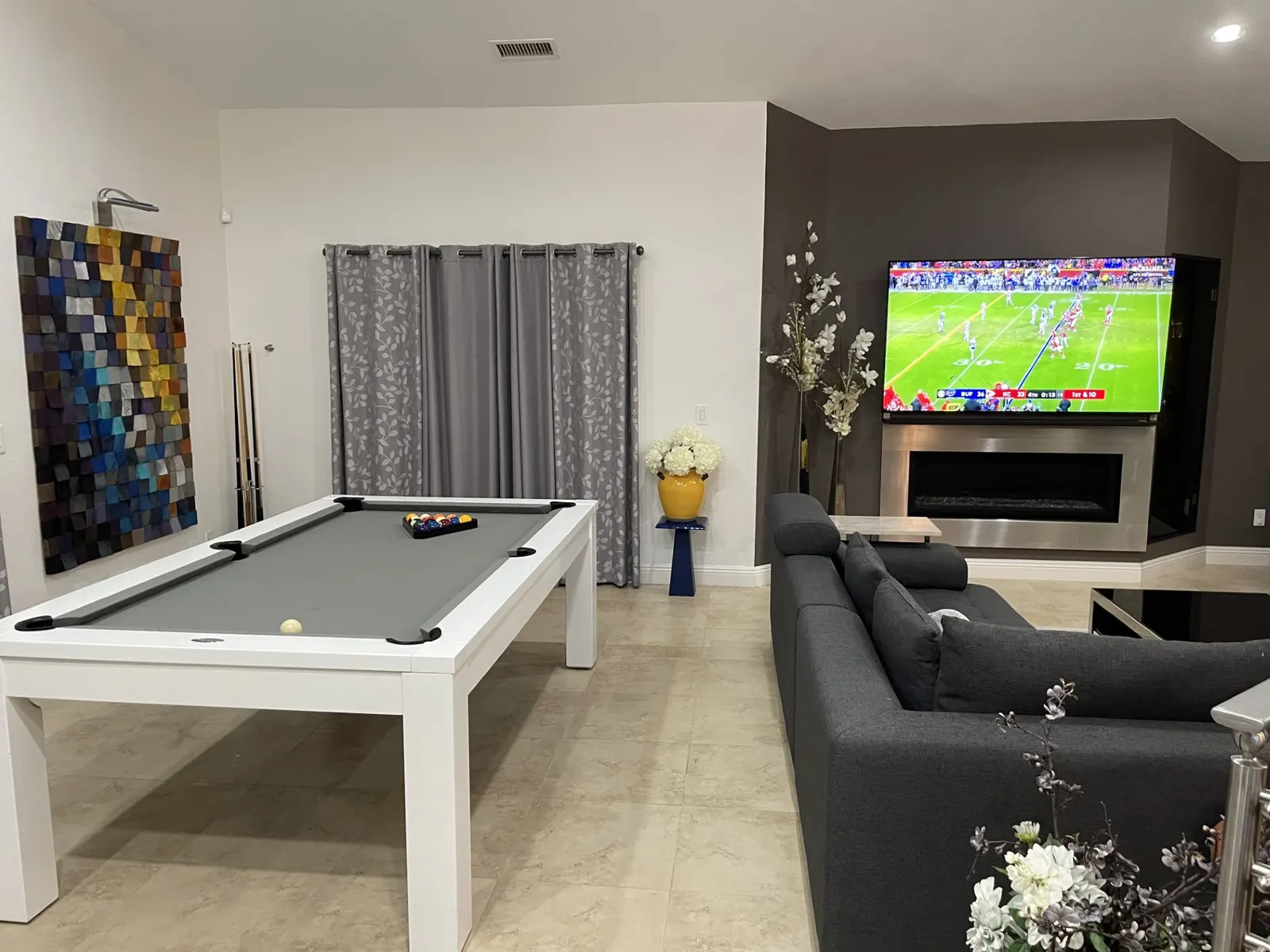 Modern living room remodel with white pool table, large TV above fireplace, and charcoal sofa.