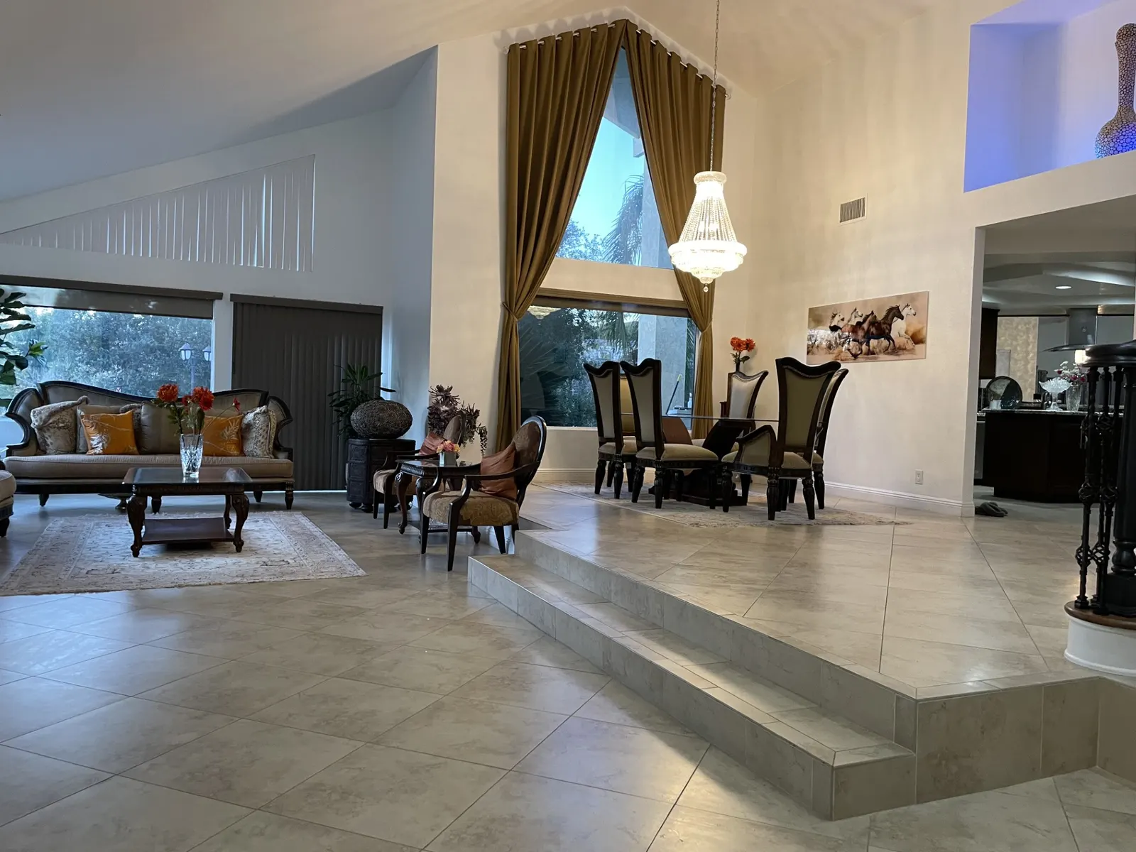 Spacious living and dining area with tiered tile flooring, large windows, chandelier, and traditional furniture.