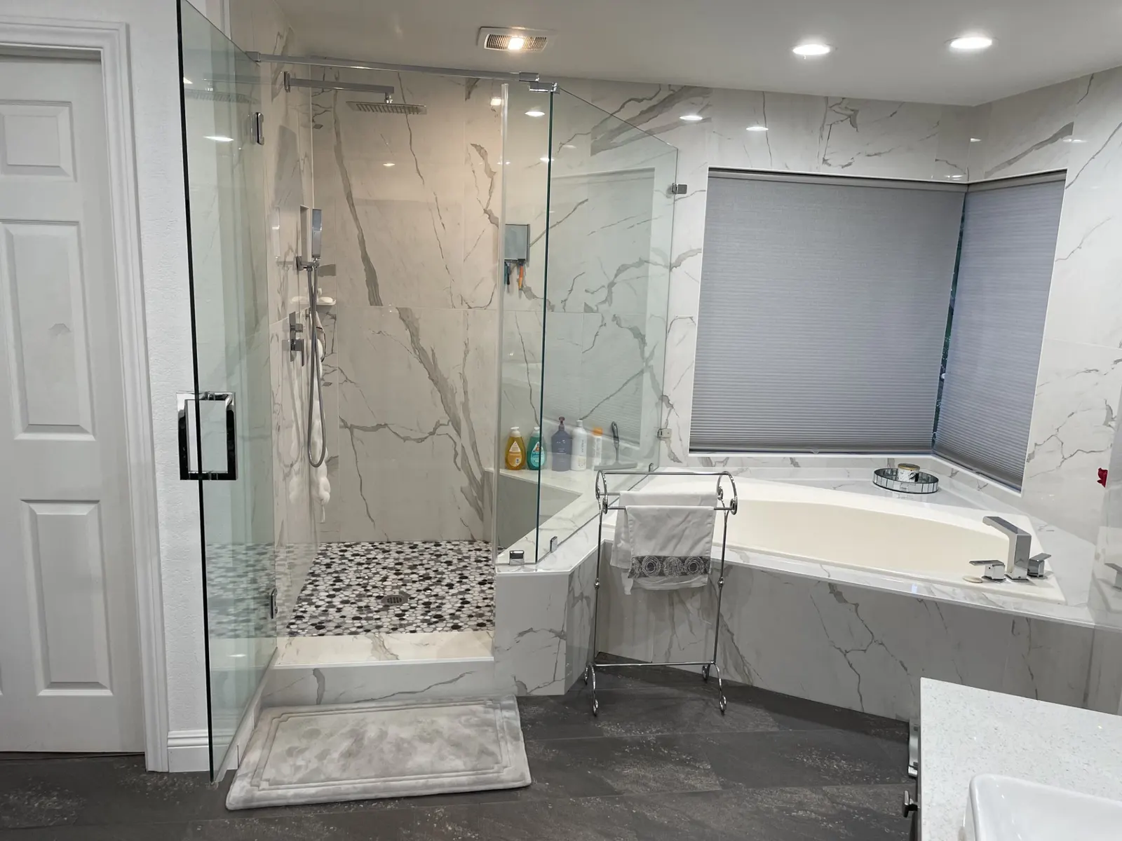 Luxurious bathroom remodel featuring Carrera marble walls, a frameless glass shower and a corner bathtub.