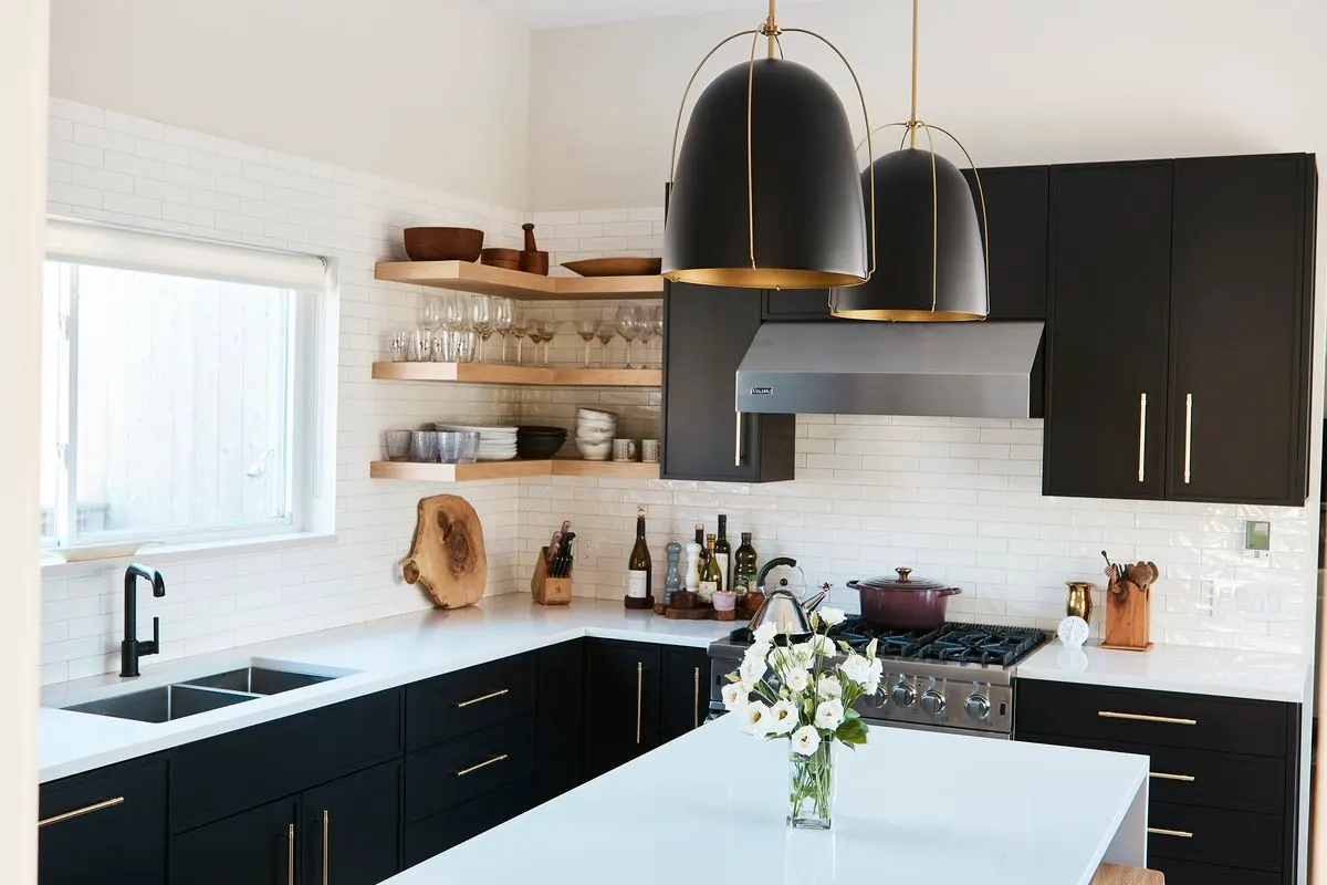 Modern kitchen with black cabinets, white countertops, subway tile, and wood open shelving. Gold accents.