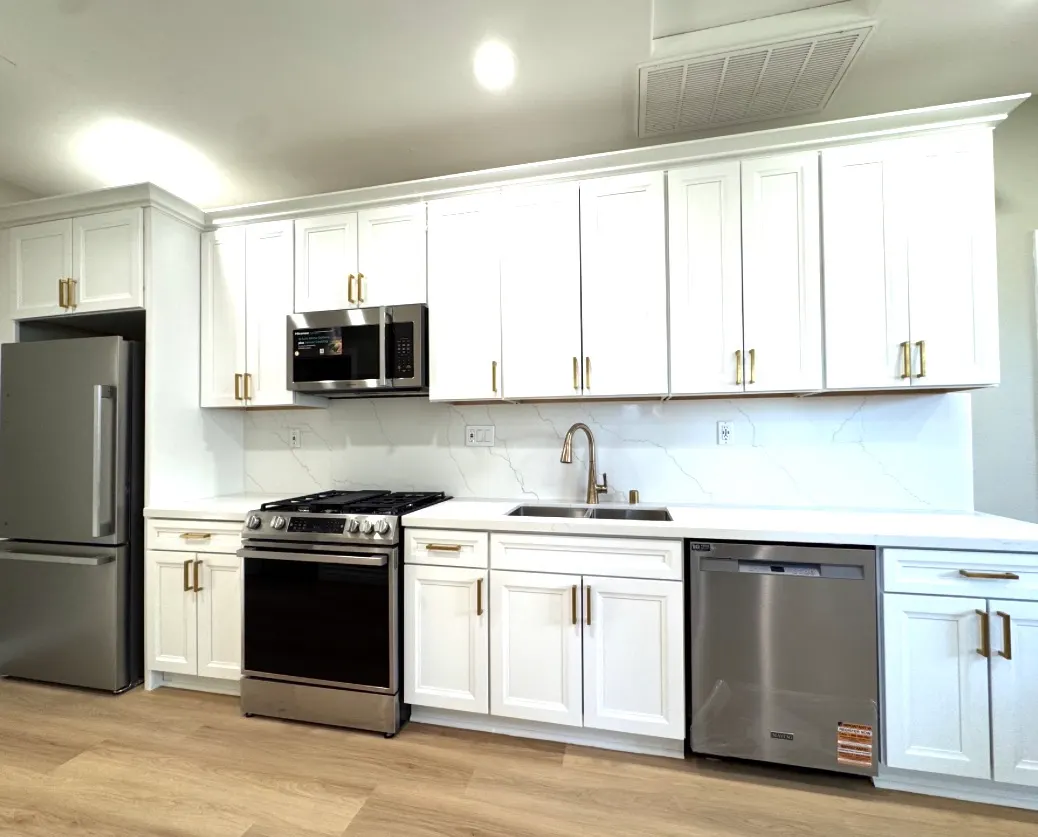 Modern white kitchen with new stainless steel appliances, white quartz countertops, and gold hardware.
