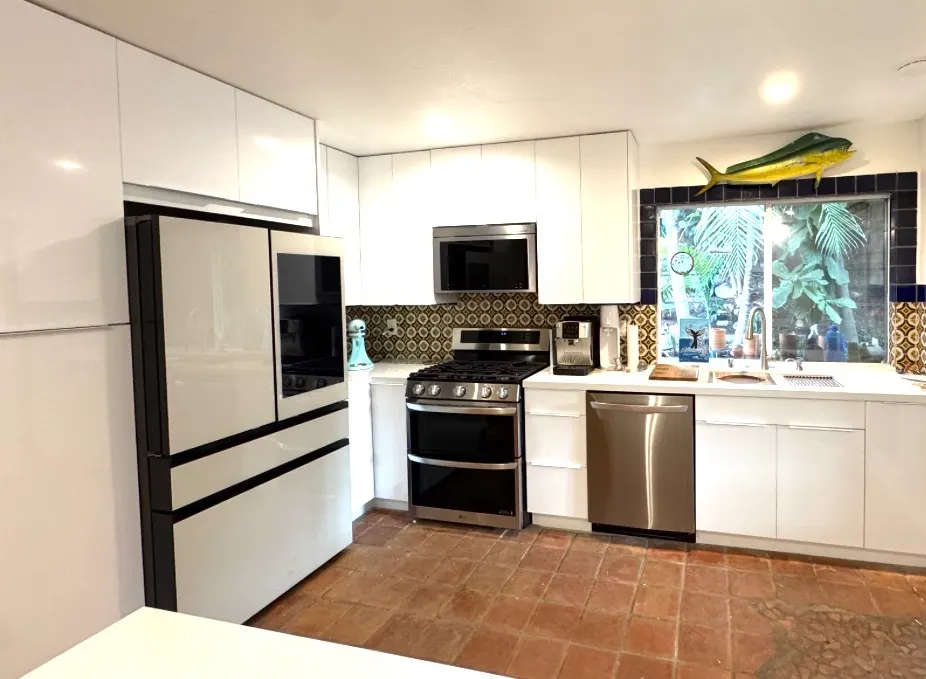 Modern white kitchen with sleek cabinets, stainless steel appliances, patterned backsplash, and terra cotta tiled floor.