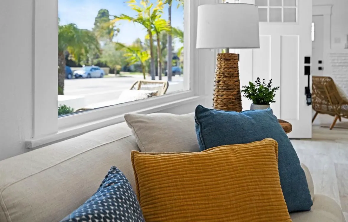 Cozy living room with plush pillows and a modern woven lamp, overlooking a sunny street.