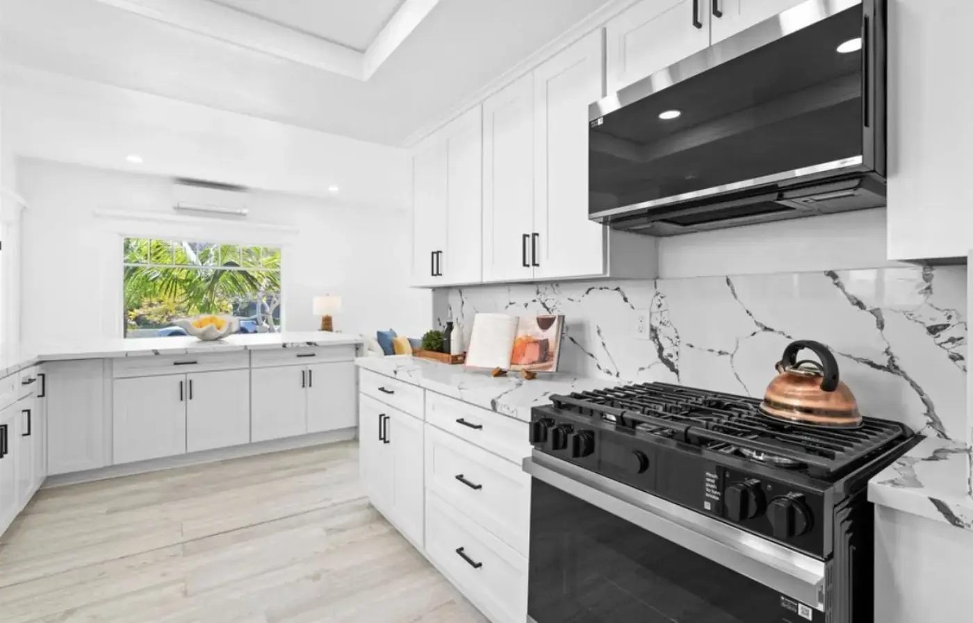 Bright white kitchen with dramatic Calacatta marble backsplash, black hardware, gas range, and breakfast nook by the window