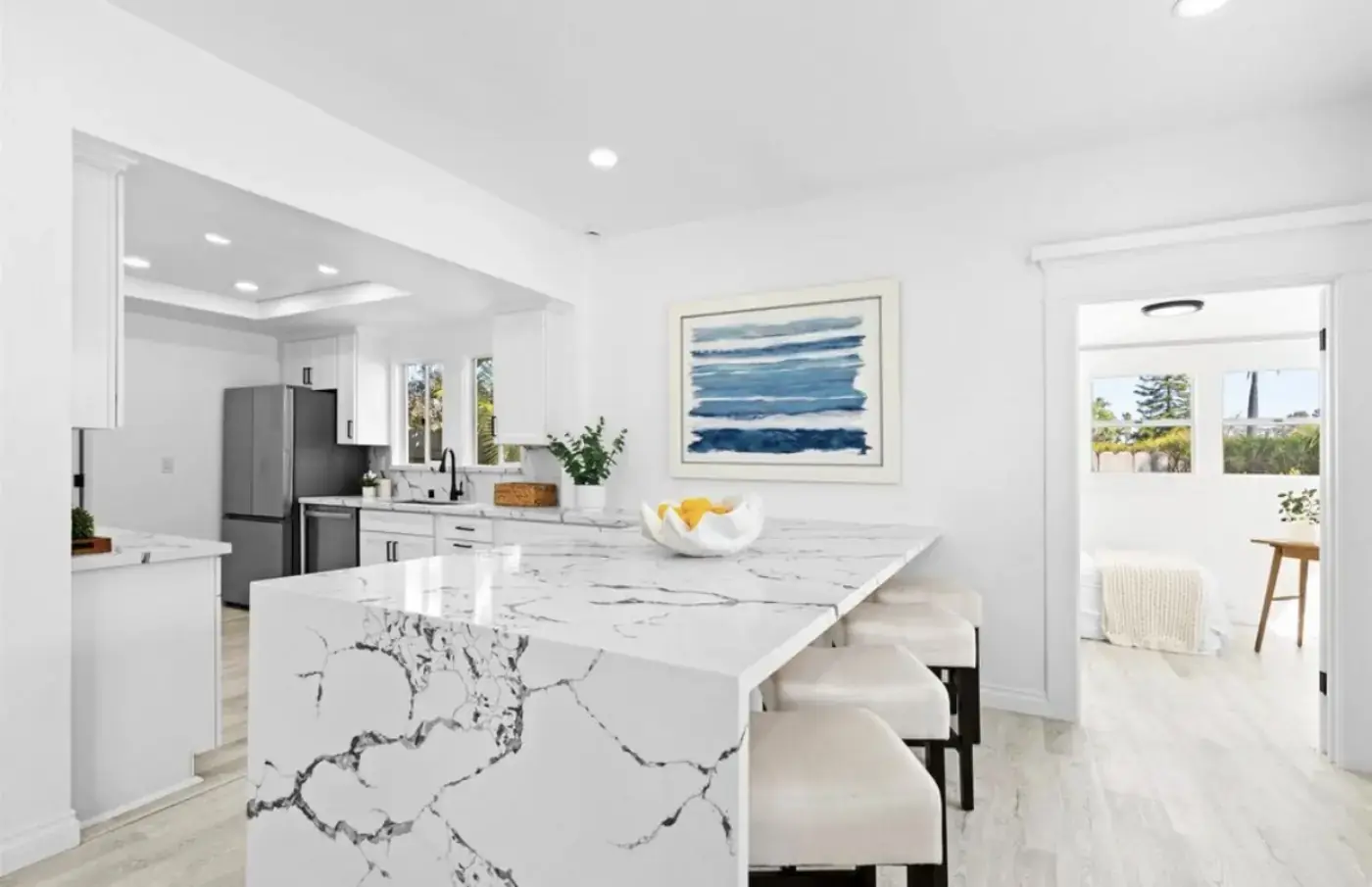 Bright open-concept kitchen with marble waterfall island, white cabinetry, and ocean-themed coastal artwork